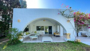 Un espace de vie extérieur moderne, avec un mur blanc, une porte en arc de cercle et des coins salon aménagés.