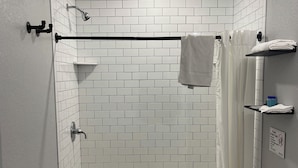 A bathroom with a shower, toilet, and sink, featuring white subway tiles and a black towel rack. - Newly remodeled 14-room hotel in charming St. Mary's . (St. Marys)