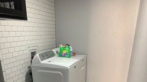 Une buanderie équipée d’un lave-linge à chargement frontal, d’une bouteille de lessive et d’une poubelle blanche.