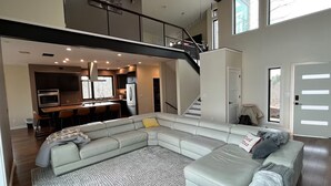 A spacious living area with a large L-shaped sectional sofa, a dining area with a bar, and a staircase leading to an upper level. - Private Mountain Top Escape  with Hot Tub, Theater, Game Room & Fire Pit (Marshall)