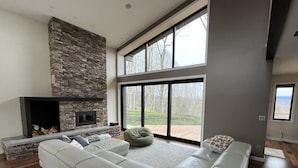 A modern living room with a stone fireplace, large windows, and a sectional sofa. - Private Mountain Top Escape  with Hot Tub, Theater, Game Room & Fire Pit (Marshall)