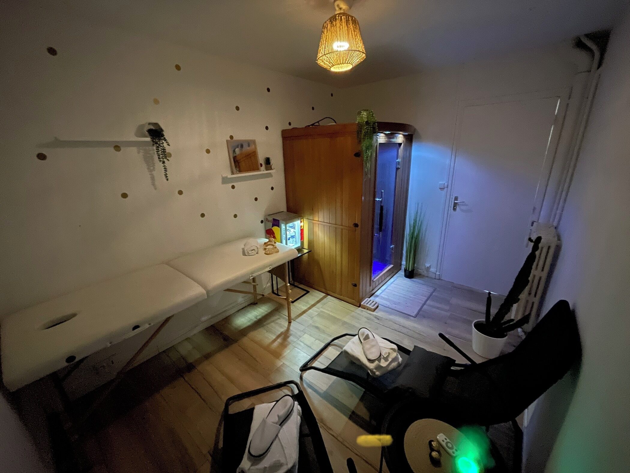 A compact living space with a wooden bench, a small table, a chair, a hanging light fixture, and a door leading to a bathroom.