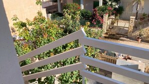 Ein Balkon mit weißen Geländern, der auf einen Garten mit verschiedenen Pflanzen und ein Gebäude mit rotem Ziegeldach blickt.