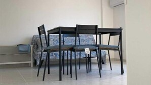 Ein Essbereich mit Tisch und vier Stühlen, einer Bank und einem gemusterten Sofa im Hintergrund.