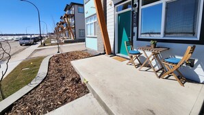 A residential building with a modern design, featuring a concrete patio with outdoor furniture and a small garden area.