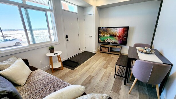 A modern, compact living space with a large window, a flat-screen TV, a dining area, and a cozy seating area.