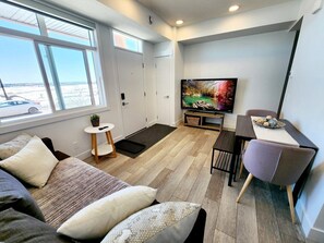 En moderne, kompakt opholdsstue med stort vindue, fladskærms-tv, spiseplads og hyggelig siddekrog.