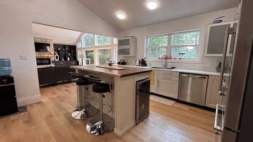 A modern kitchen with a central island, bar stools, a refrigerator, and a dishwasher.