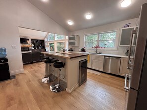 A modern kitchen with a central island, bar stools, a refrigerator, and a dishwasher.
