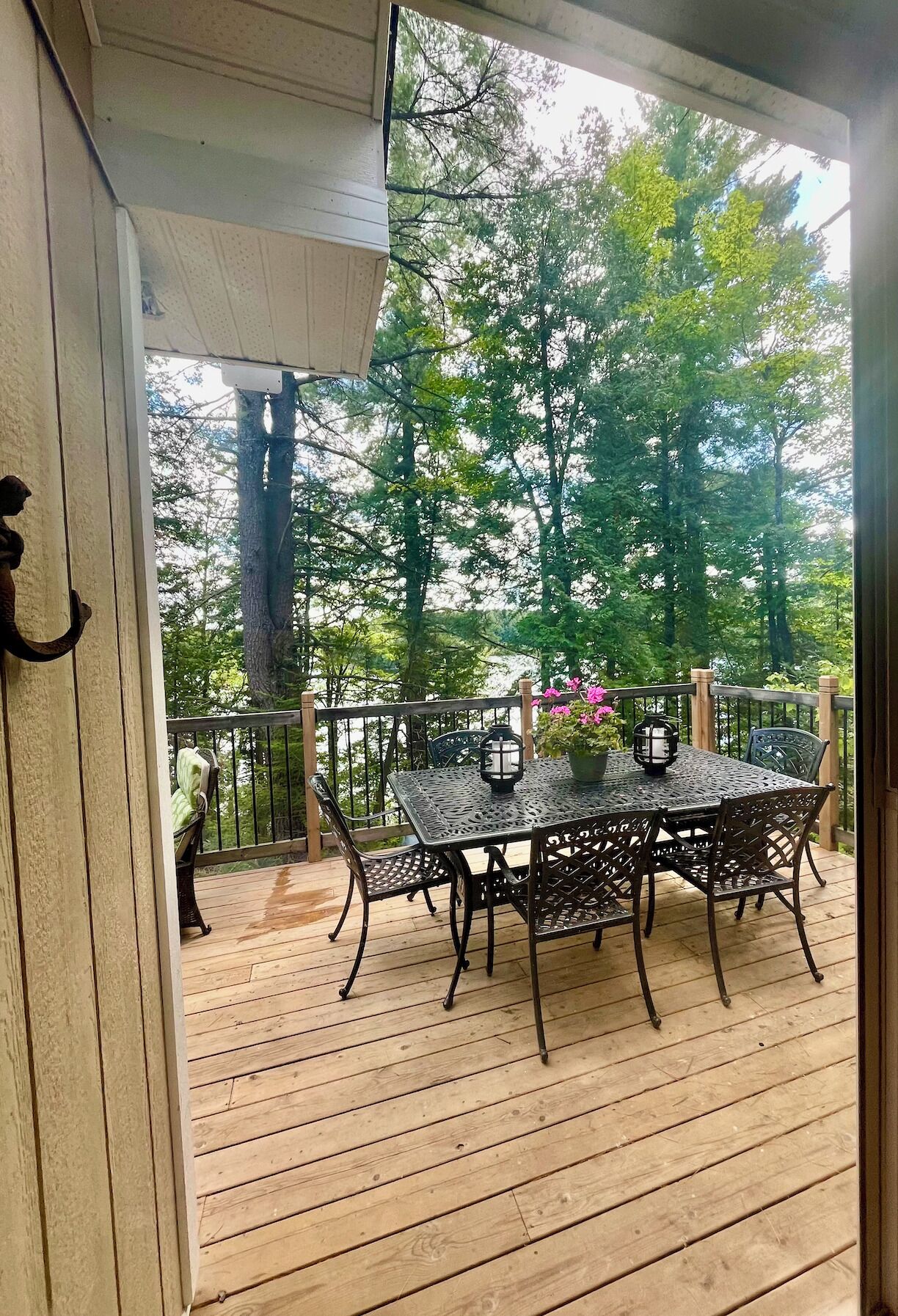 A covered outdoor deck with a wooden floor, metal table and chairs, and a railing.
