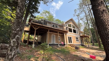 A two-story wooden house with a balcony, surrounded by trees.