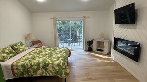 A bedroom with a bed, a ceiling fan, a TV, and a view of the outdoors.