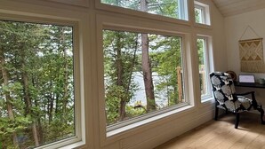 A room with large windows offering a view of a forest and a lake. There is a chair and a desk with a laptop.