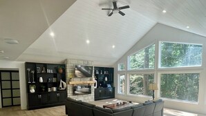 A spacious living area with a large dark sofa, a stone fireplace, and a ceiling fan.