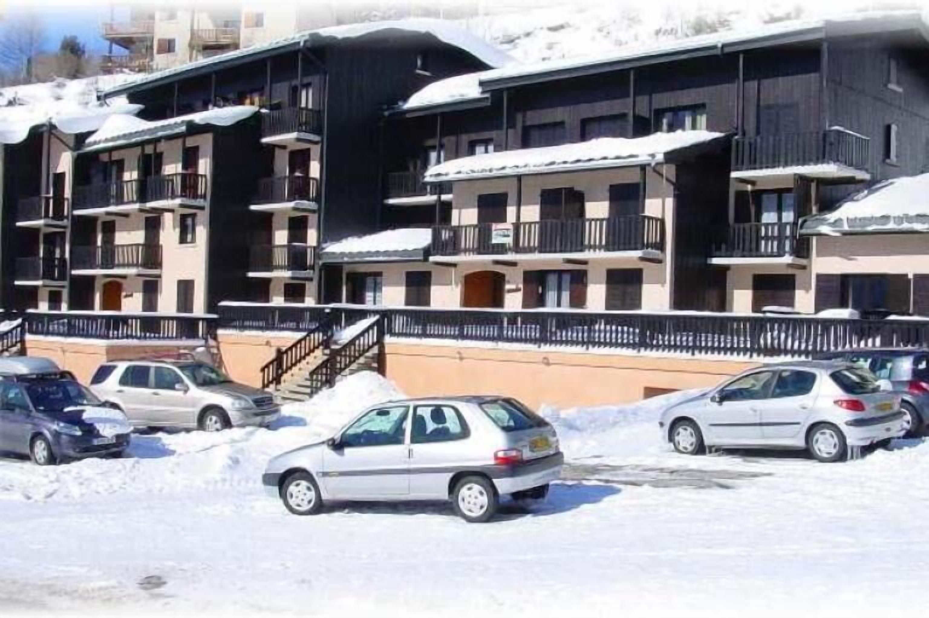 Un immeuble à plusieurs étages, doté de balcons, avec des voitures garées et de la neige sur le toit.