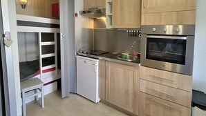 A compact kitchen with wooden cabinets, a built-in oven, a sink, and a small refrigerator.