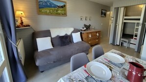 A cozy living room with a sofa, a dining table set for two, and a painting on the wall.