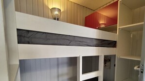 A bunk bed with a headboard, a shelf above, and a wardrobe with a red panel.