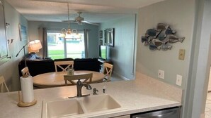 A compact kitchen with a sink, a dishwasher, and a dining area with a table and chairs. - Ocean View Ground Floor 2/2 (New Smyrna Beach)