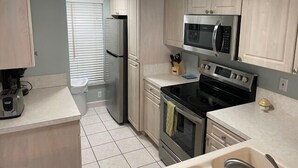 A modern kitchen with stainless steel appliances, light wood cabinets, and a tiled floor. - Ocean View Ground Floor 2/2 (New Smyrna Beach)