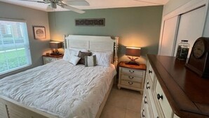 A bedroom with a bed, nightstands, a dresser, a ceiling fan, and a window with blinds. - Ocean View Ground Floor 2/2 (New Smyrna Beach)