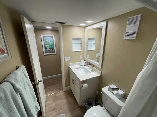 A bathroom with a white sink, mirror, and toilet. There is a towel rack and a picture on the wall.