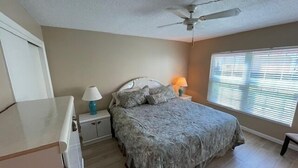 Un dormitorio con cama, mesitas de noche, ventilador de techo y ventana con persianas.