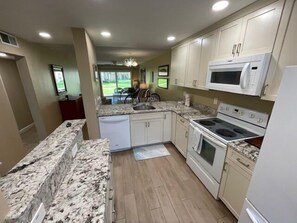 A kitchen with white cabinets, a granite countertop, a microwave, a stove, and a dishwasher.