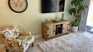 Ein Wohnzimmer mit einem sternenmusterigen Sessel, einer Holzkommode mit Dekoration, einer großen Wanduhr und einer Topfpflanze.