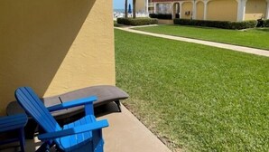 Eine Terrasse mit blauen Stühlen und einem Tisch, ein gepflegter Rasen und im Hintergrund ein Gebäude mit rotem Dach.