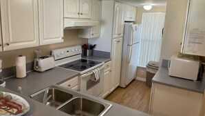Una cocina con armarios blancos, un fregadero de acero inoxidable, una estufa y un refrigerador.