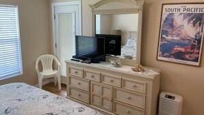 Un dormitorio con cama, cómoda, televisor, silla y un cartel en la pared.