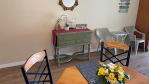 Un comedor con una mesa de madera, dos sillas, un aparador verde, un espejo y un adorno en la pared.