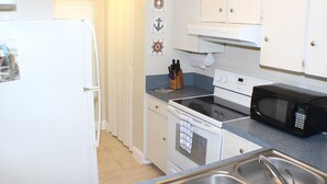 A kitchen with white cabinets, a stove, a microwave, and a sink.