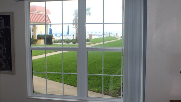 A bedroom with a large window overlooking a well-maintained lawn and a distant view of a building with a red roof.