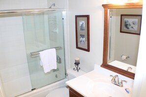 Une salle de bain avec une douche à parois de verre, un lavabo blanc avec un miroir et des tableaux encadrés accrochés au mur.