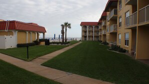 A hotel with a red roof, a grassy lawn, and a view of the beach.