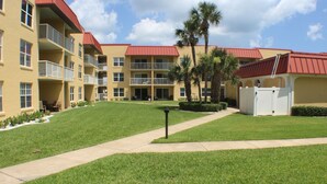 A multi-story hotel with balconies, a well-maintained lawn, and a clear sky. - Ocean View Ground Floor 2/2 (New Smyrna Beach)