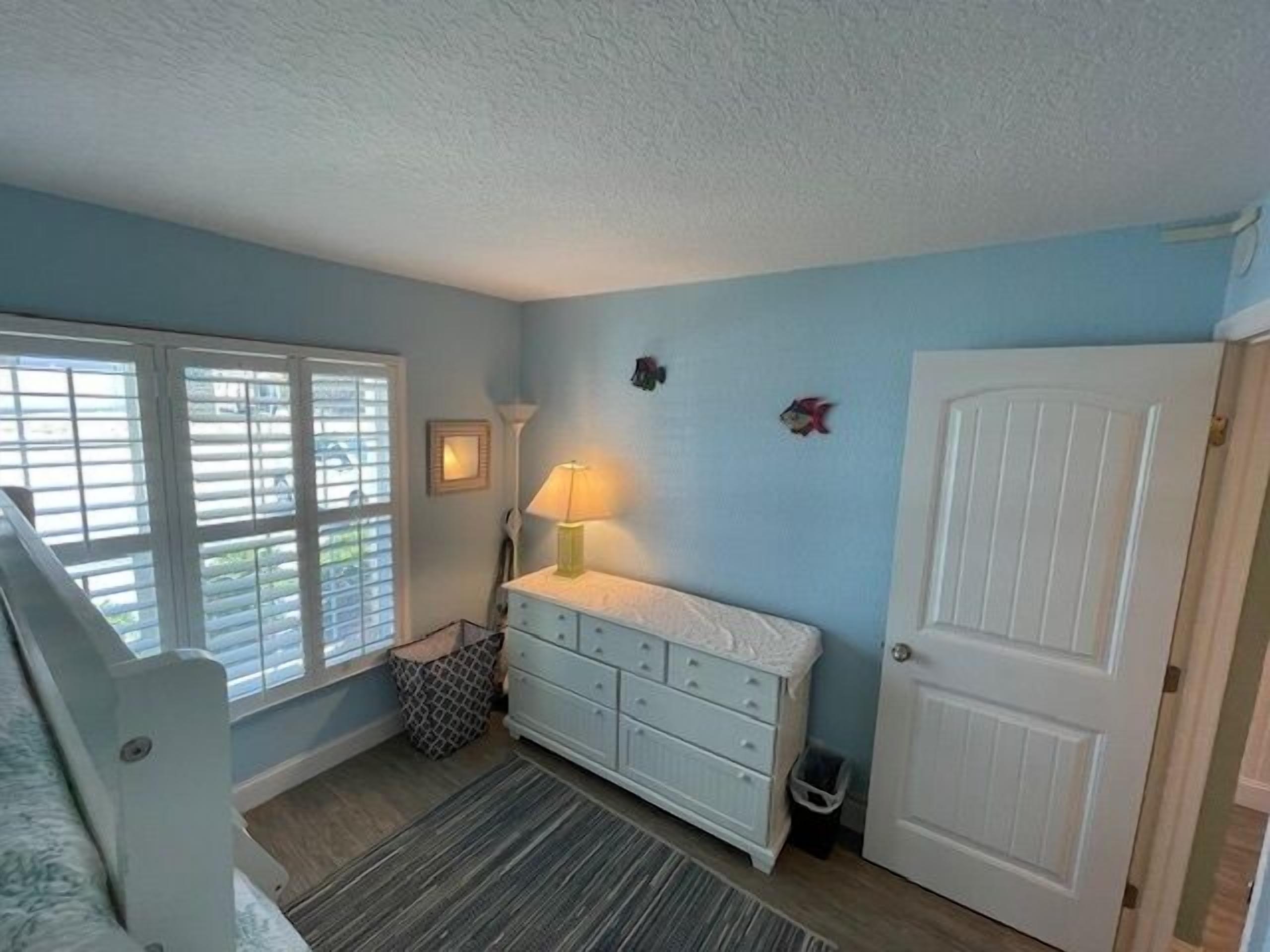 A room with a window, a dresser, a lamp, and a door.