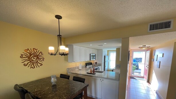 A dining area with a marble table and chairs, a chandelier, and a sun art piece on the wall. - Ground Floor Ocean View 2/2 (New Smyrna Beach)