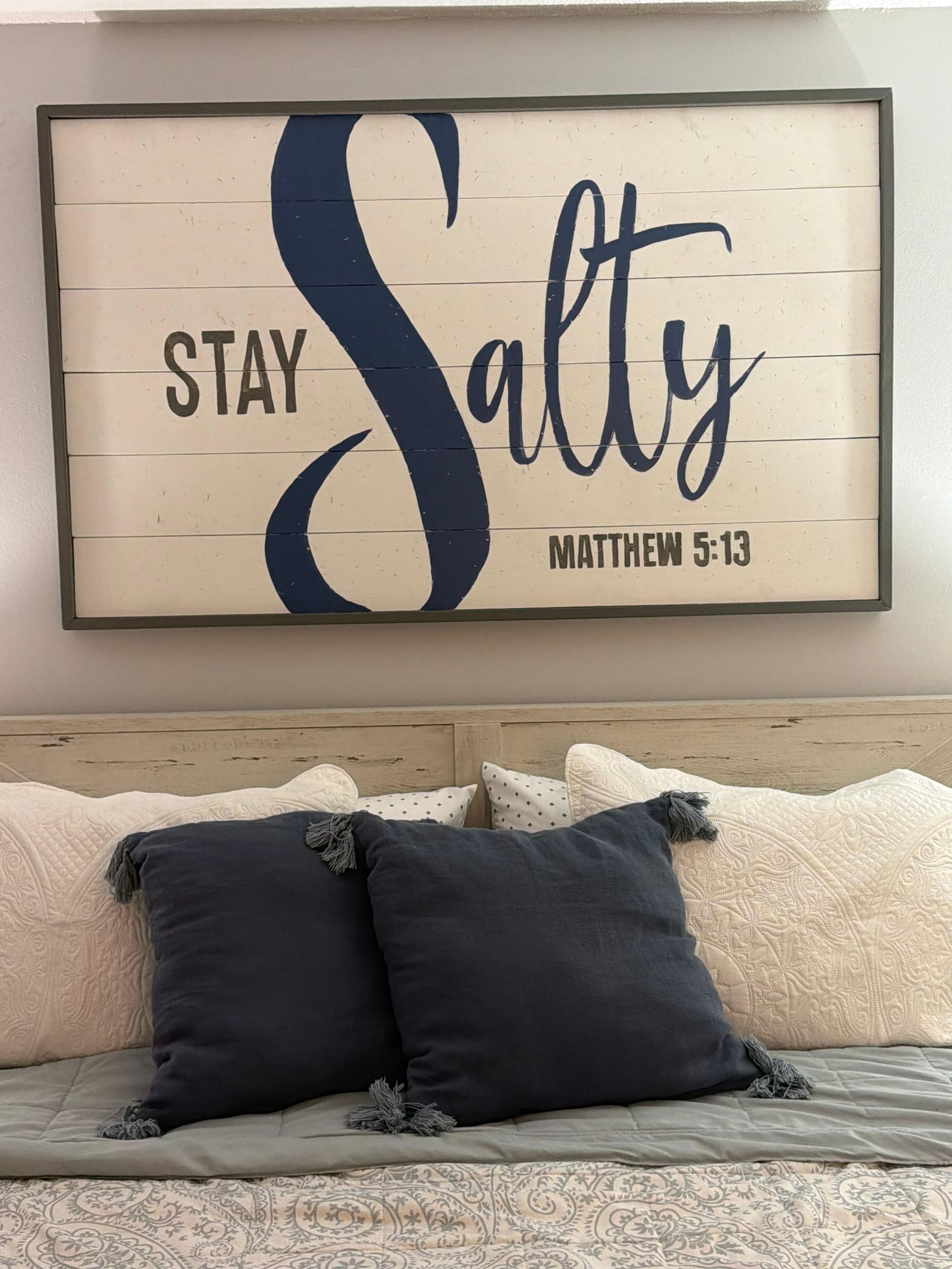 Een lijst met een motiverende quote op een muur, boven een bed met beddengoed met een patroon en donkere kussens.