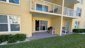 Un edificio residencial de varios pisos con techo plano, balcones y un pequeño patio con mobiliario exterior.