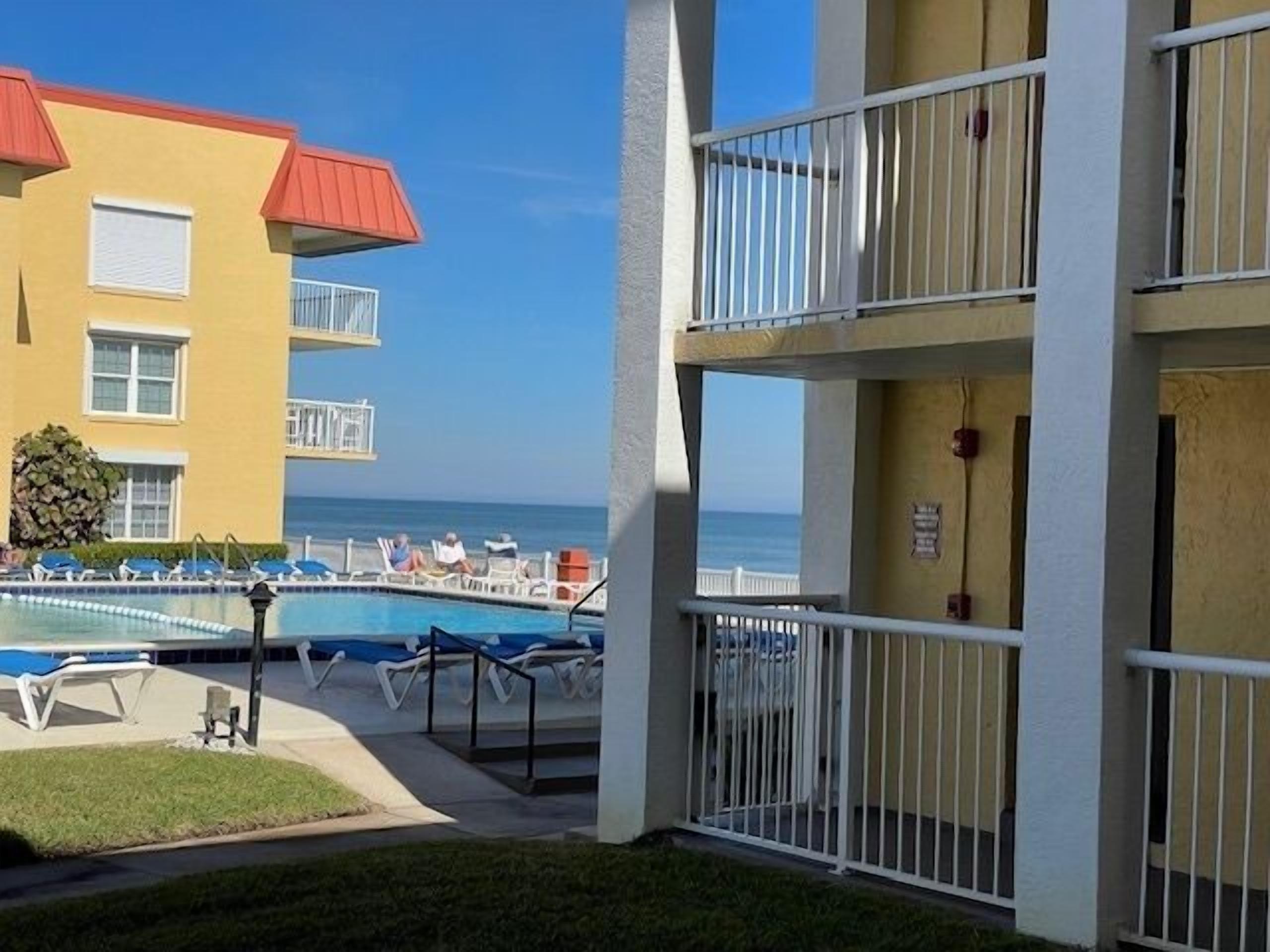A hotel with a pool area, lounge chairs, and a view of the ocean.