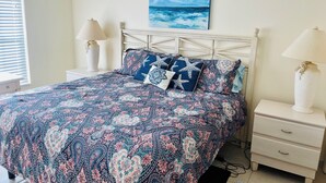 Een slaapkamer met een bed, nachtkastjes en een schilderij van de zee.