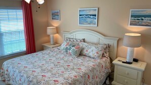 Une chambre à coucher avec une couvre-lit à motifs floraux, deux lampes de chevet, un ventilateur de plafond et trois tableaux encadrés accrochés au mur.