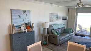 Ein Wohnzimmer mit einer Couch, einem Esstisch, einem Schrank und Blick auf den Strand.