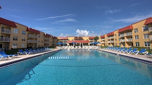 Ein Swimmingpool mit blauen Liegestühlen und Sonnenschirmen, umgeben von mehrstöckigen Gebäuden mit Balkonen.