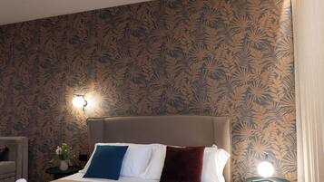 A neatly made bed with rolled towels, a bedside table with a lamp, and a patterned wallpaper.