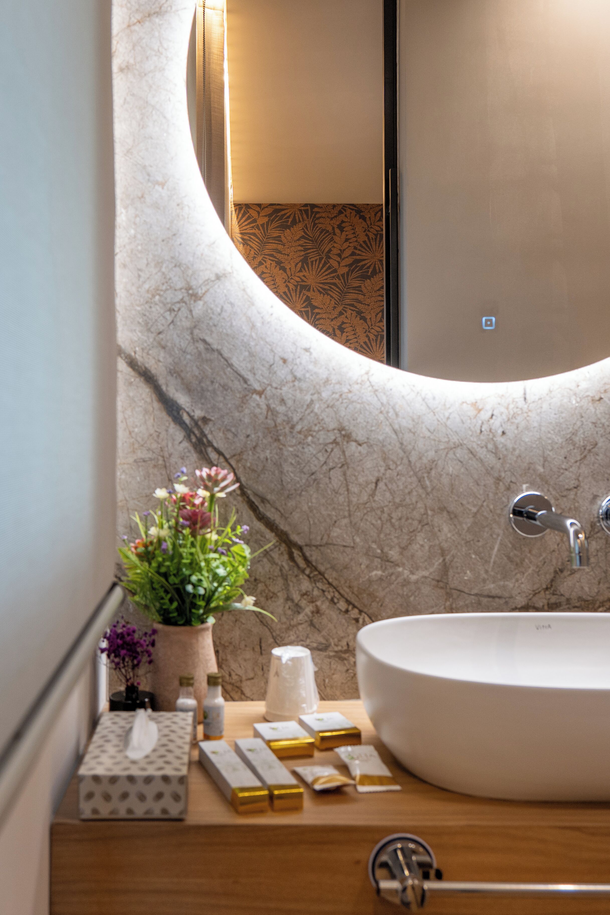 Un bagno con un lavandino in marmo curvo, un mobile contenitore in legno e uno specchio.