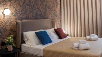 A modern hotel room with a large bed, a nightstand with a vase of flowers, and a window with vertical blinds.